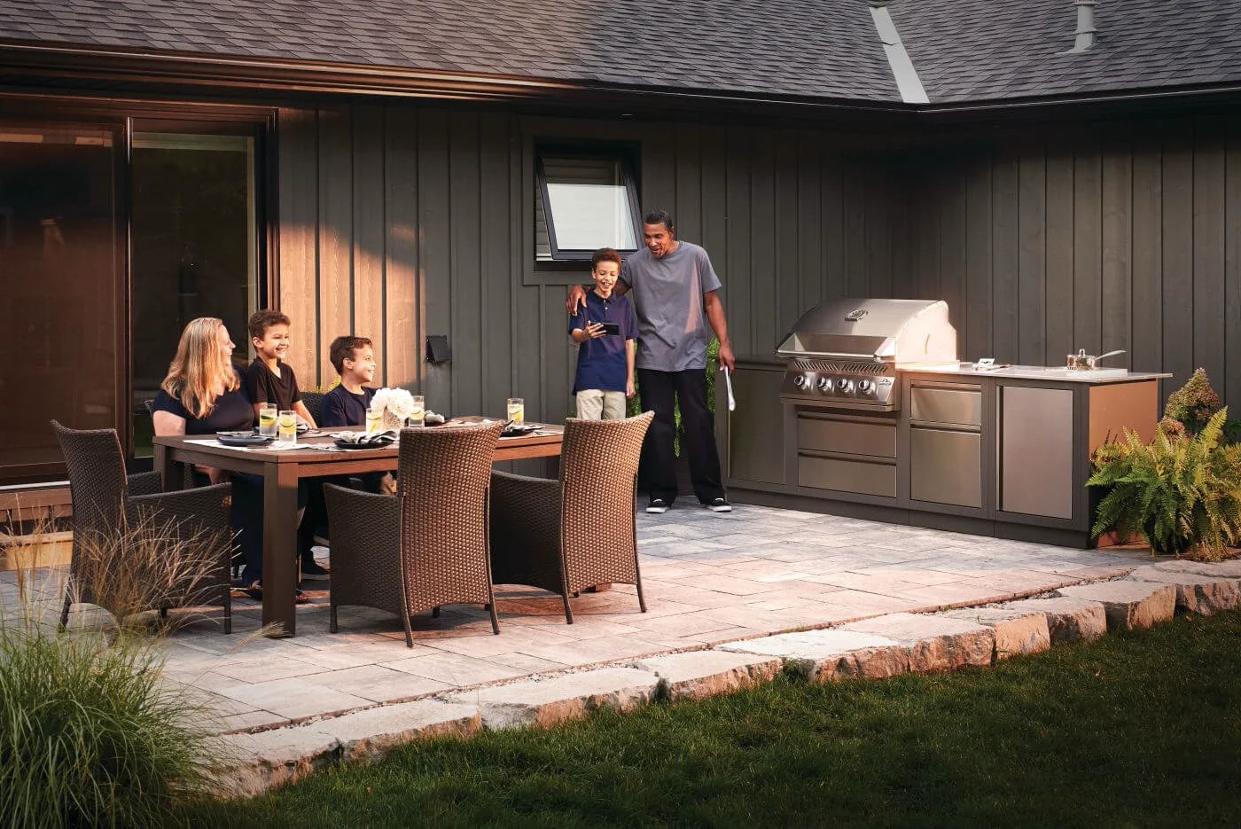 Family gathered around a dining table on a patio with a Napoleon 500 Series Built-In gas grill in the background
