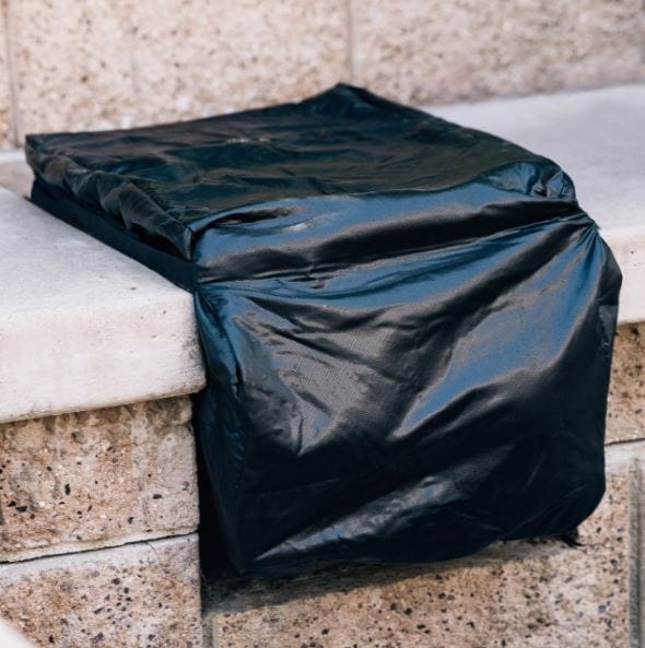 Black weatherproof cover draped over an outdoor kitchen appliance, protecting it from rain, dust, and UV exposure.