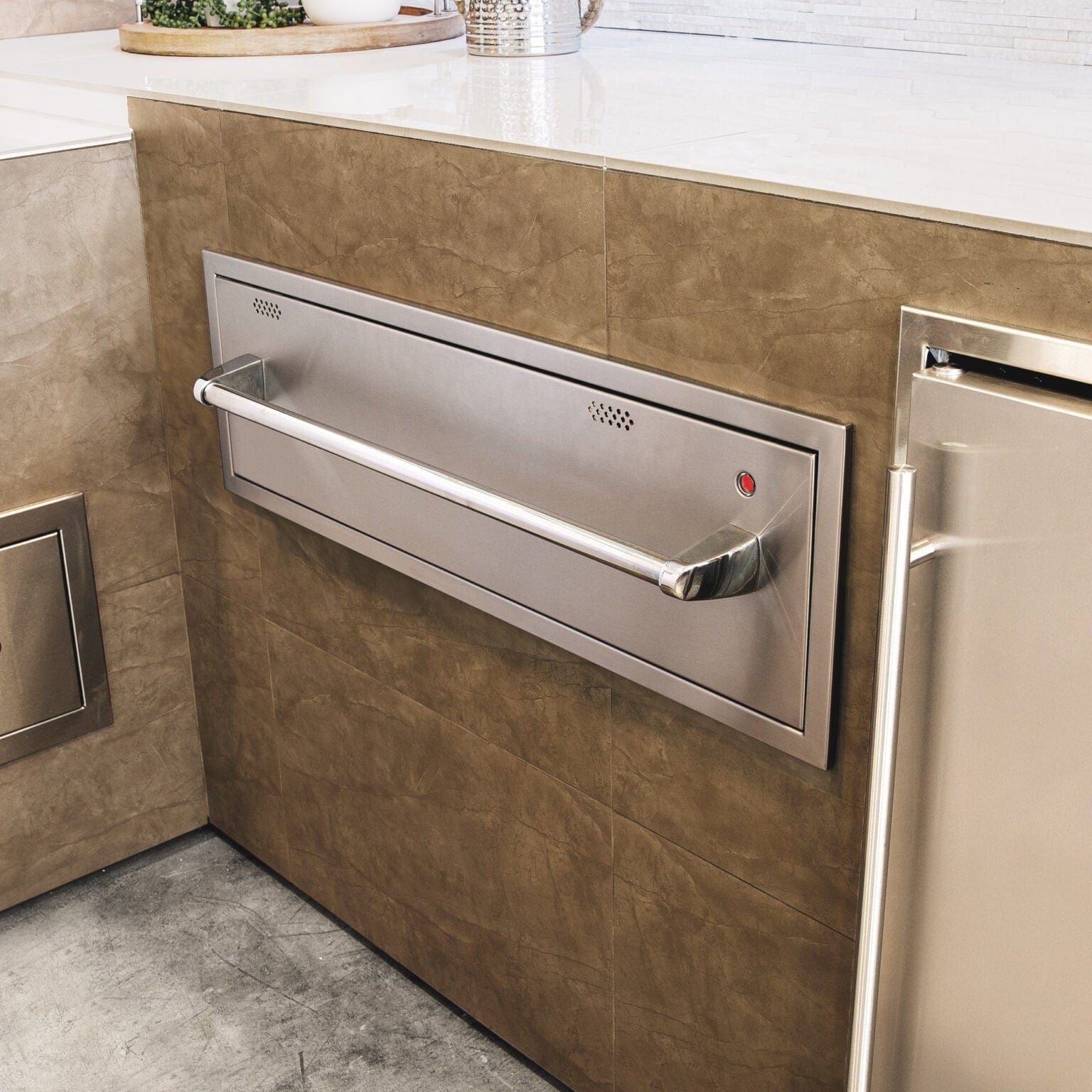 Built-in stainless steel outdoor warming drawer installed in a kitchen island with sleek handle and indicator light.