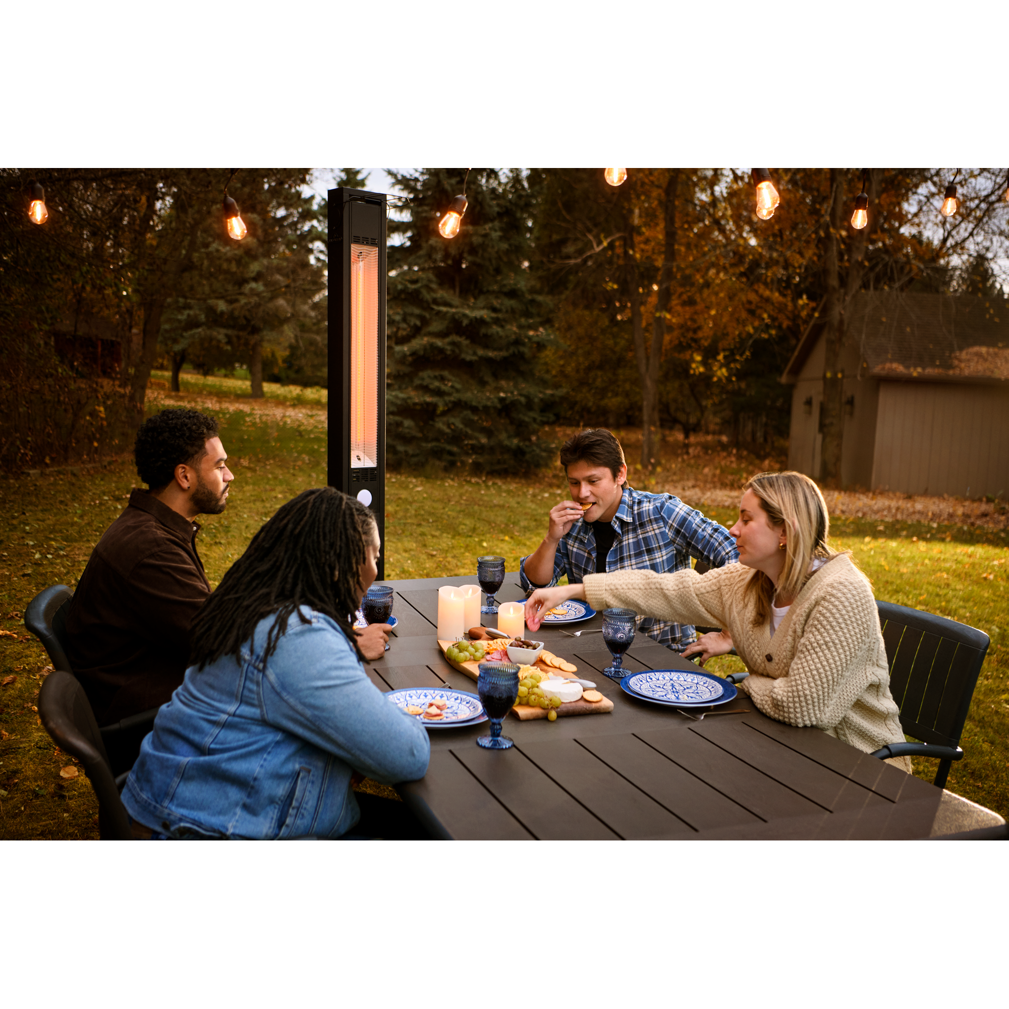 People sitting around an outdoor table with a Napoleon Phantom Infrared Electric Heater in the background.